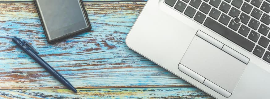 przycięte zdjęcie stołu na którym znajduje się laptop oraz telefon