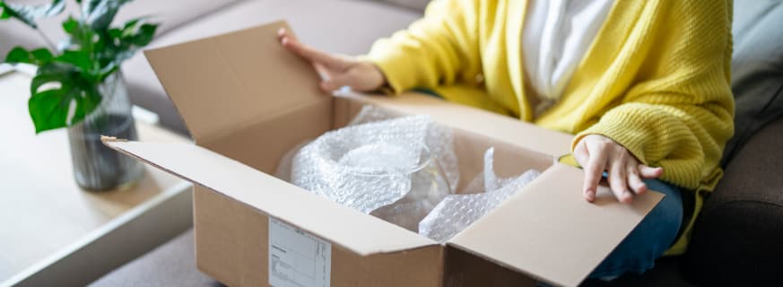 Kobieta otwiera kartonowe pudełko z produktami zabezpieczonymi folią bąbelkową.
