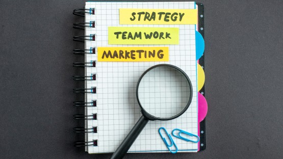 Notatnik z kartkami "Strategy", "Team Work", "Marketing" na kolorowych karteczkach.