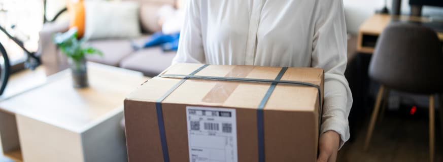 Kobieta w białej koszuli trzyma kartonowe pudełko z etykietą.
