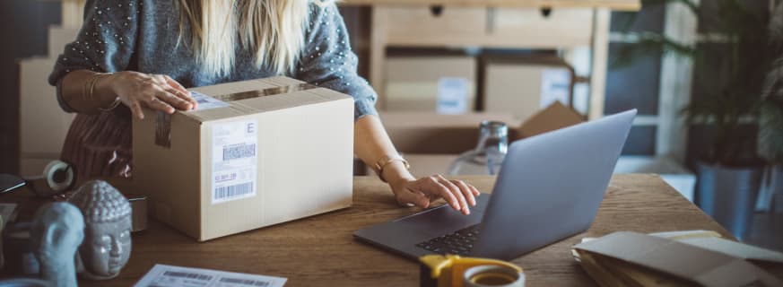 Kobieta pakuje paczkę i korzysta z laptopa.