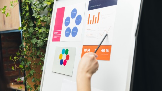 Prezentacja z wykresami i diagramami na tablicy, osoba wskazuje wykres liniowy.