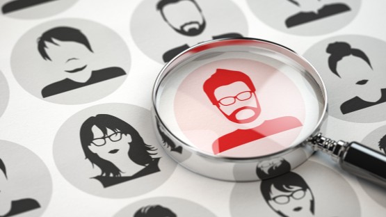 Lupa powiększa profil czerwonego mężczyzny wśród czarno-białych sylwetek.