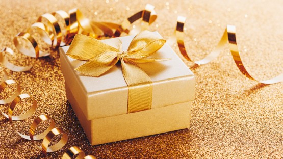 Złote pudełko z kokardą na tle złotych ozdobnych wstążek.