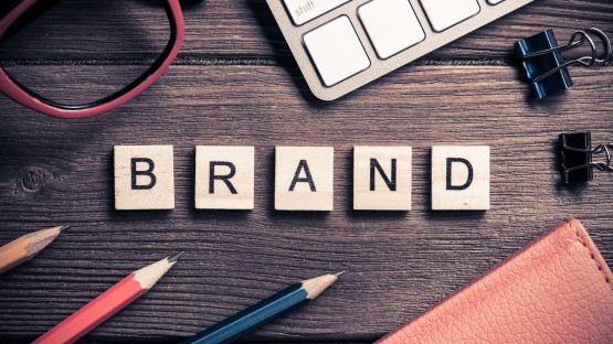 Drewniane kostki z napisem "BRAND" na stole, obok okularów i klawiatury.