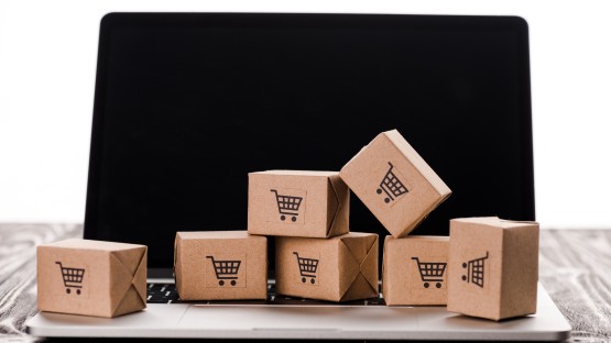 Kartony z symbolami koszyka na laptopie, symbolizujące zakupy online.