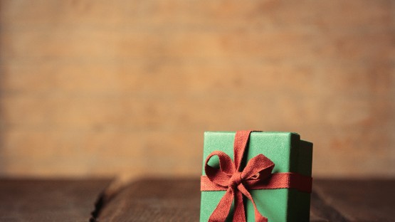 Zielone pudełko z czerwoną wstążką na drewnianym stole, tło rozmyte.