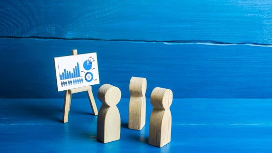 Wykresy i diagramy na sztaludze, obok trzy drewniane figurki ludzi.