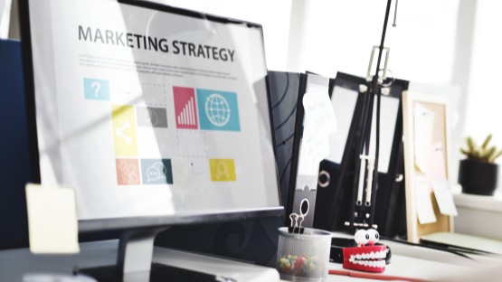 Ekran komputera z grafiką o e-commerce retailer, biurowe akcesoria w tle.