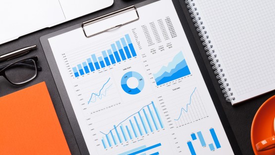 Wykresy visual marketing i diagramy na kartce papieru, okulary, notatnik, laptop, pomarańczowy kubek.