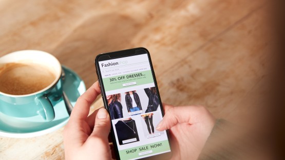 Zakupy online na telefonie, banery, a w tle filiżanka kawy i drewniany stół.