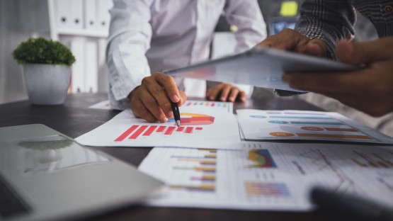 Analiza wykresów finansowych, dwie osoby przeglądają dane przy biurku z laptopem.