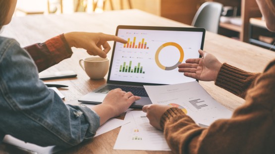 Dwie osoby analizują wykresy na laptopie podczas spotkania biznesowego.